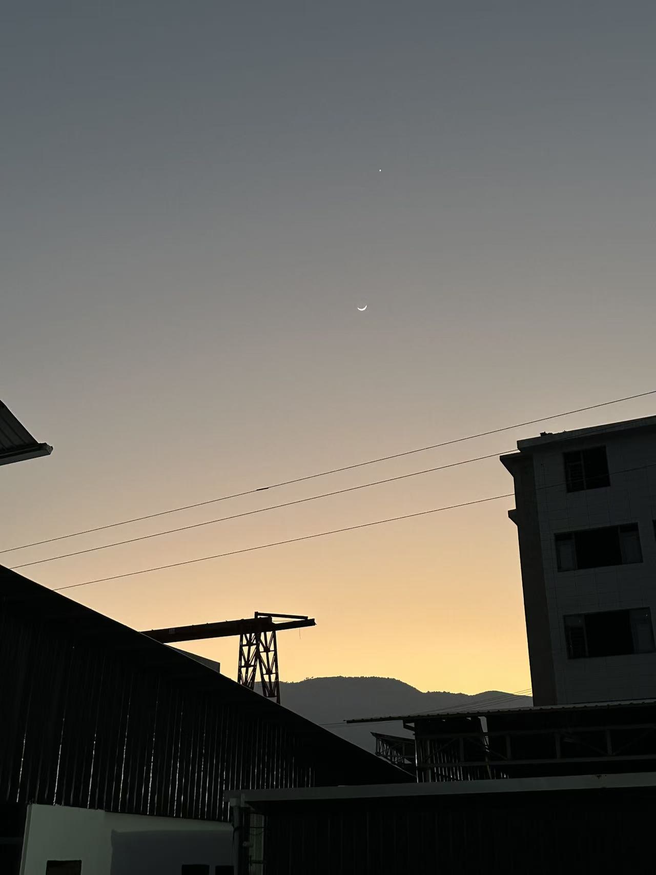 Crescent moon over buildings at sunset